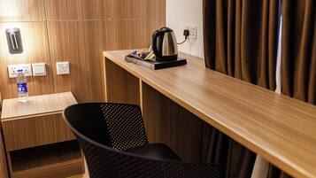 A wooden desk with a kettle, a bottle of water, and a chair.