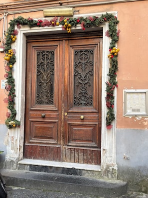 A wooden double door with intricate metalwork, flanked by a garland of greenery and red decorations. - Apartments in the heart of Naples' historic center (Napoli)