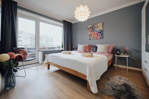 Une chambre moderne avec un grand lit, une table de chevet, une chaise, une fenêtre avec des rideaux et une vue sur la ville.