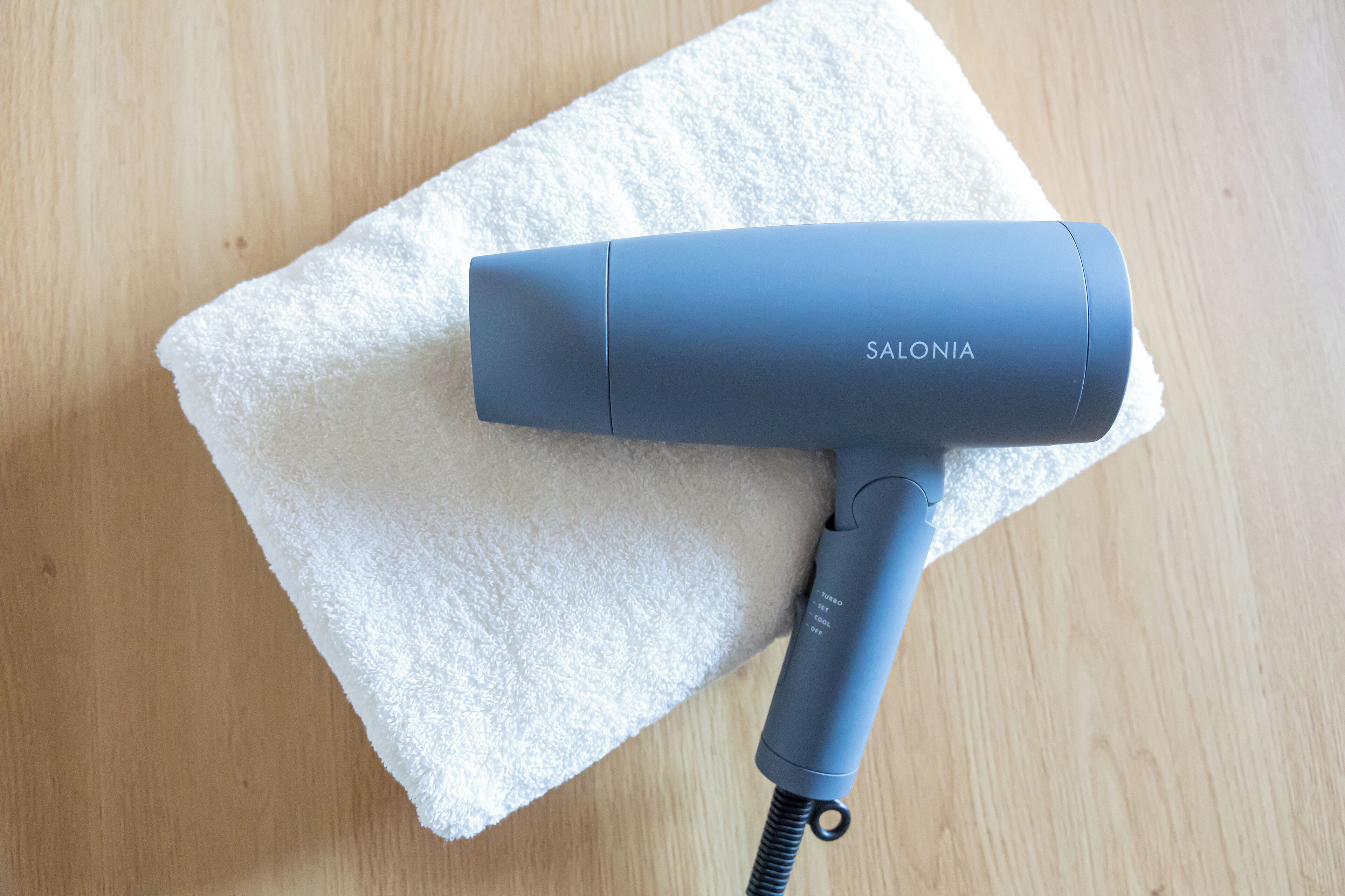 A blue hair dryer with the brand name 'SALONIA' on a white towel on a wooden surface.