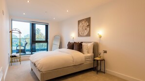 Een slaapkamer met een groot bed, een raam met uitzicht, een nachtkastje met lamp en een kunstwerk aan de muur.