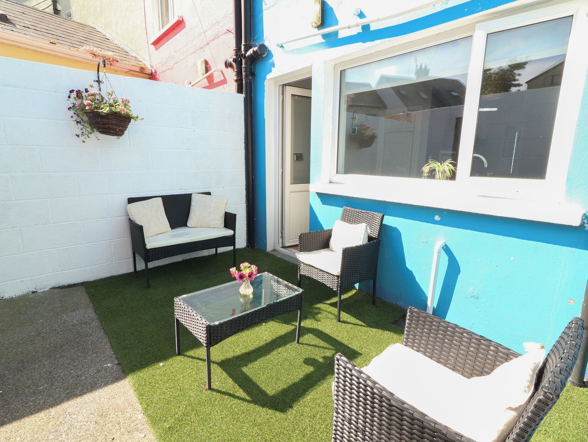 Un patio con un sofá, dos sillones, una mesa de vidrio y césped artificial.