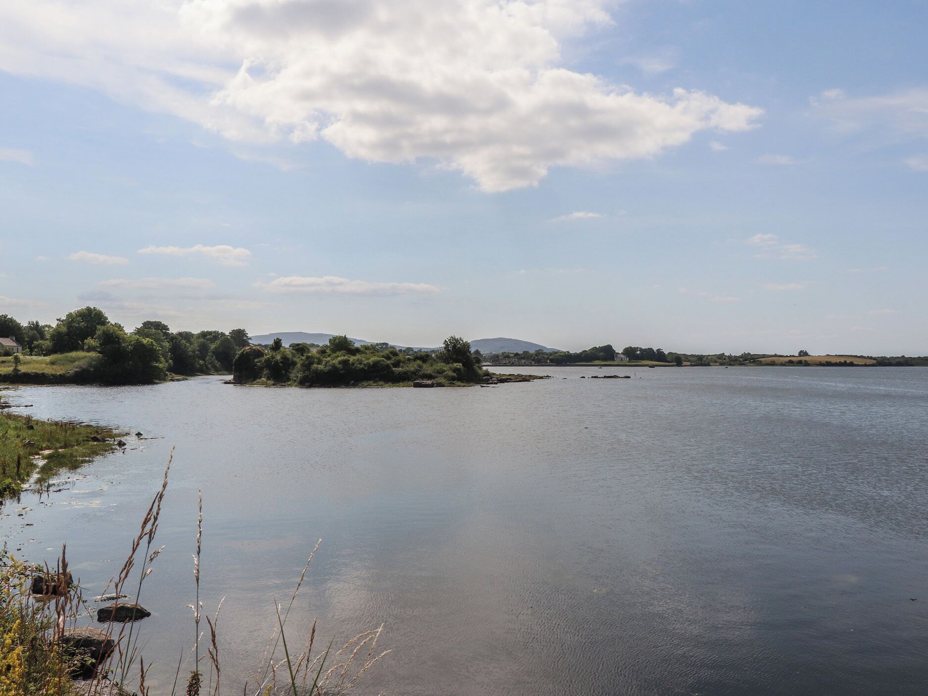 Une rivière paisible, avec une petite île et des collines qui se dessinent à l’horizon.