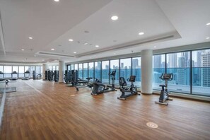 A spacious gym with various exercise equipment and large windows offering a city view. - StayShort - Modern 1BR in Prime Business Bay 4 Guests (Business Bay)