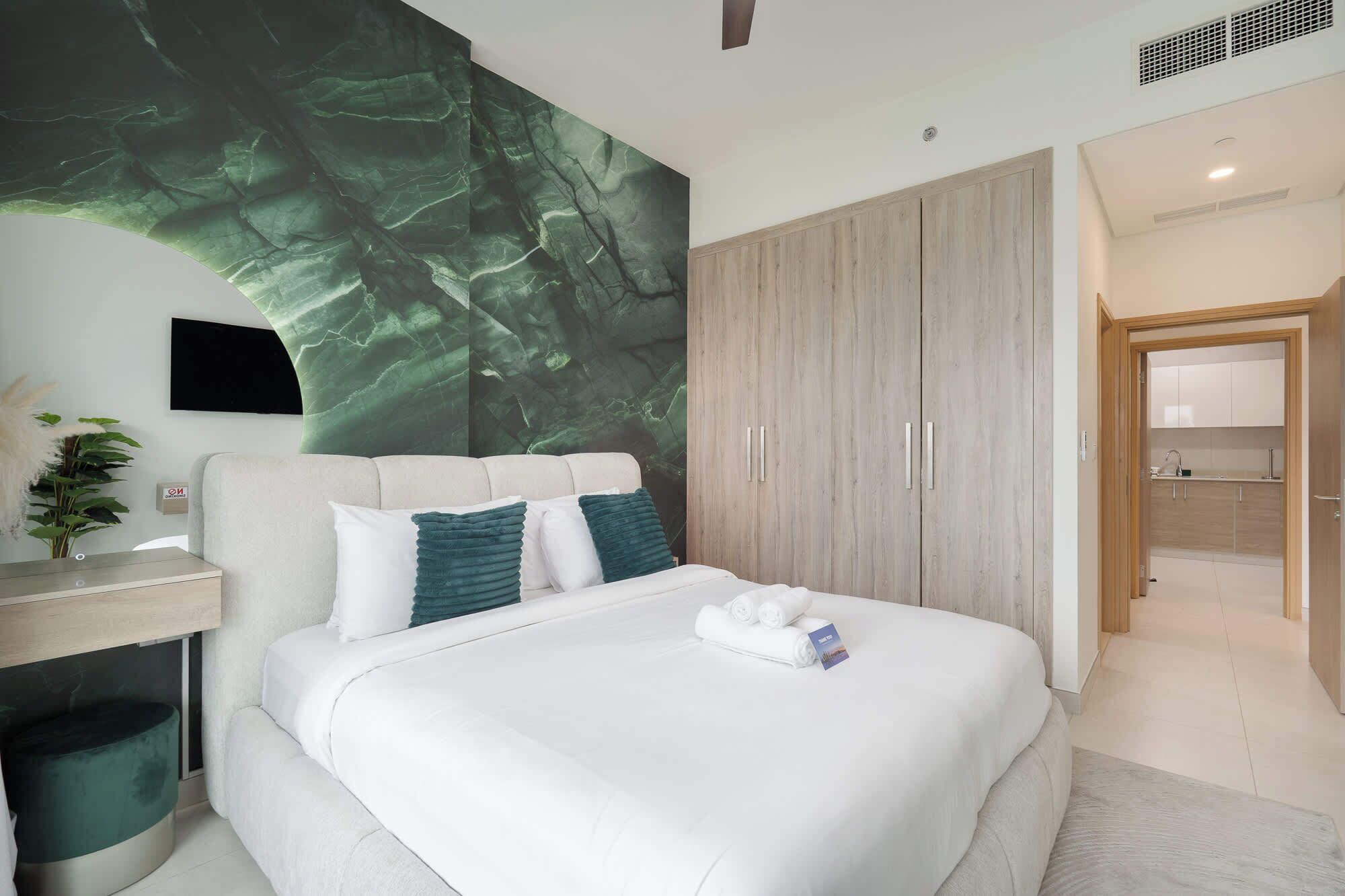Een moderne hotelkamer met een groot bed, een houten garderobe, een bureau met stoel, en uitzicht op de badkamer.