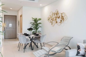 A modern dining area with a round table, grey upholstered chairs, and a decorative wall piece. - StayShort - Modern 1BR in Prime Business Bay 4 Guests (Business Bay)