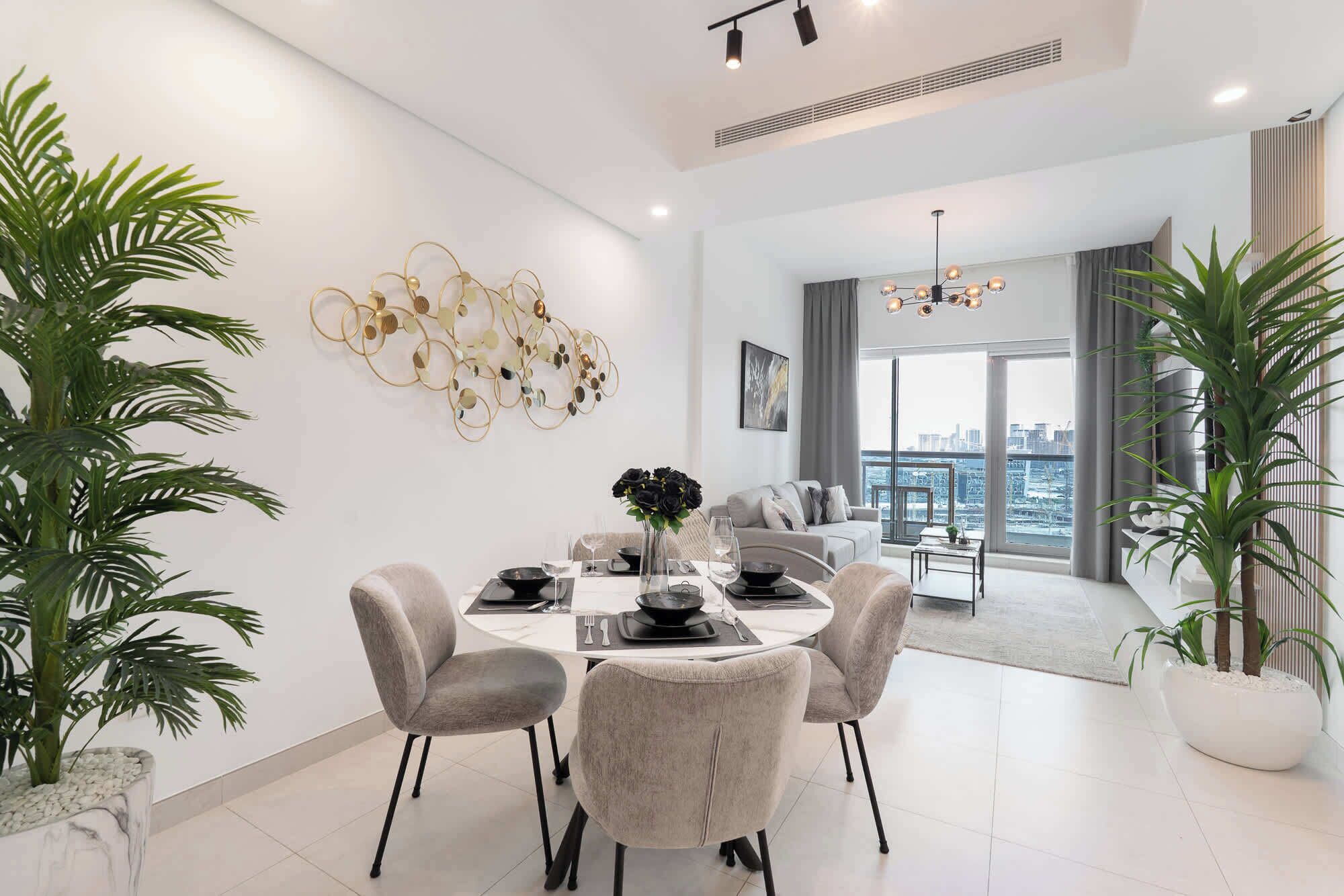 A modern dining area with a round table, grey upholstered chairs, and a decorative wall piece.