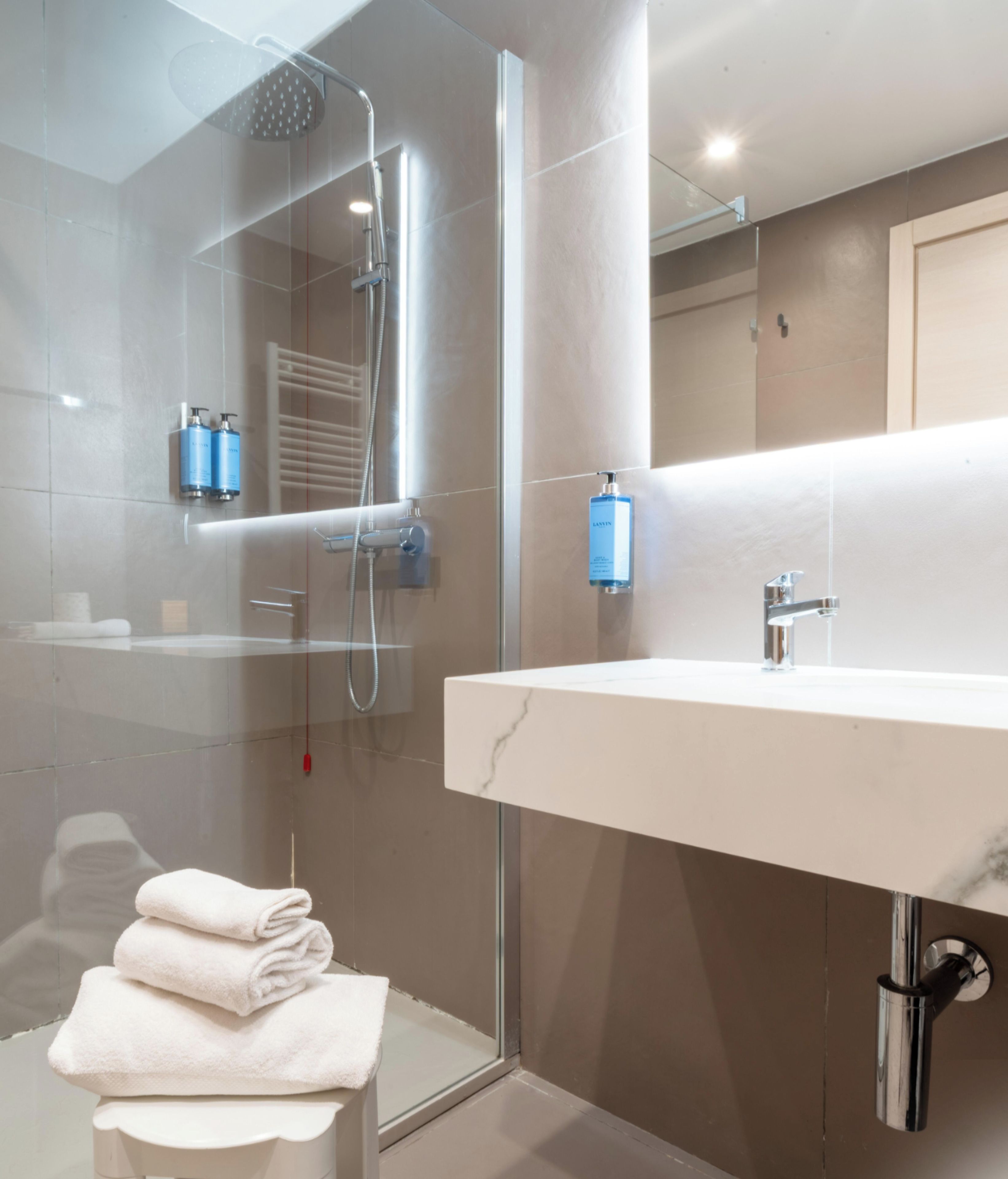 Un baño moderno con ducha envuelta en cristal, lavamanos de mármol blanco y espejo sobre el lavamanos.