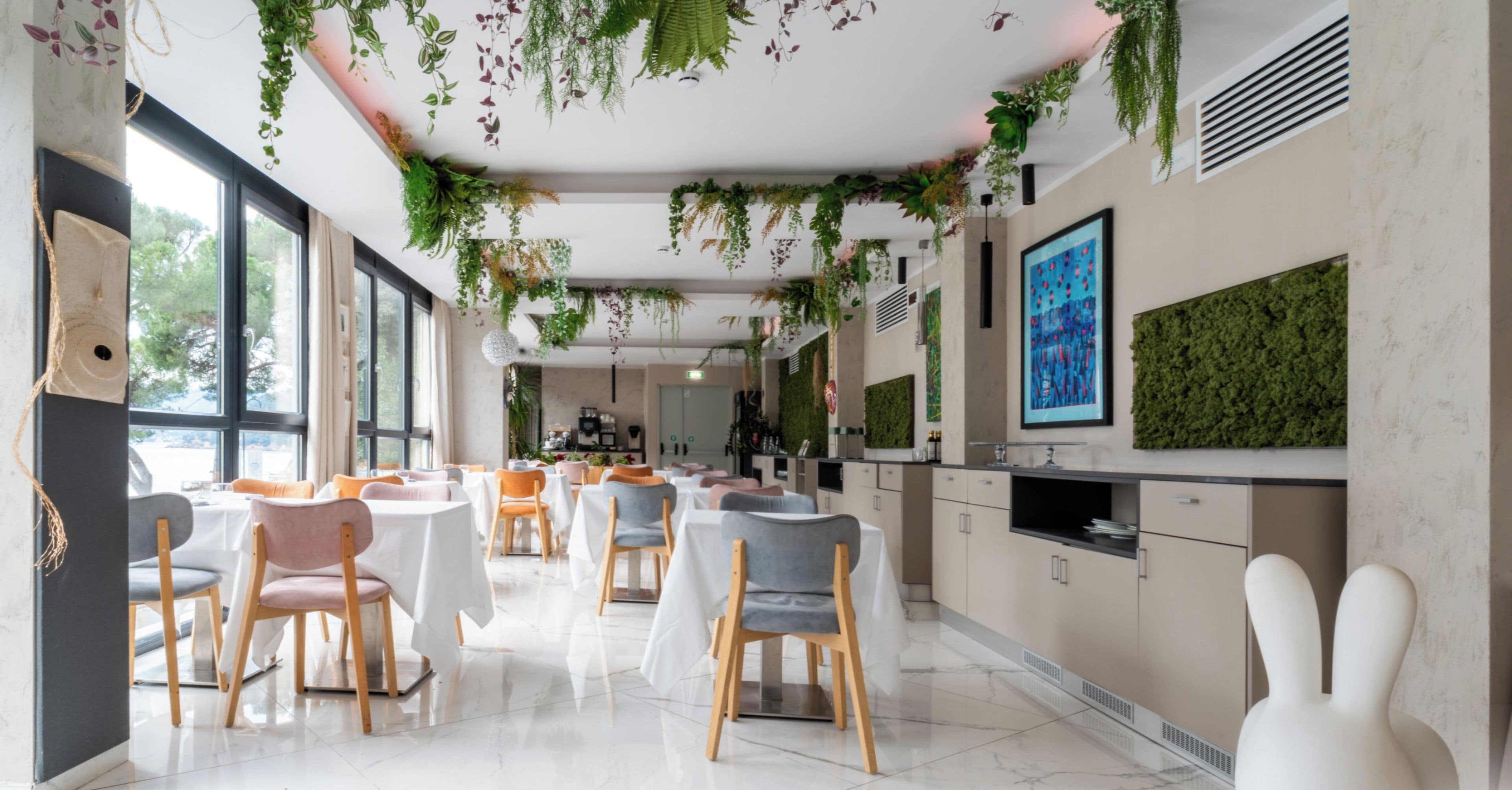 A modern dining area with tables and chairs, a kitchen area, and a large window providing natural light.