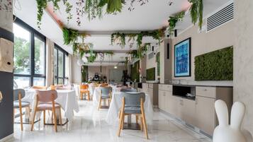A modern dining area with tables and chairs, a kitchen area, and a large window providing natural light.