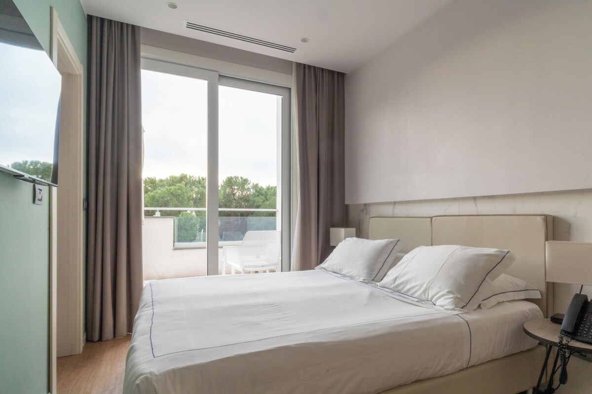 Habitación de hotel con una cama grande, una mesita de noche con lámpara y vistas al exterior a través de una puerta corrediza.