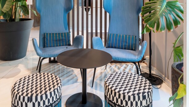 Un moderno vestíbulo de hotel con dos sillones tapizados en azul, una mesa redonda y otomanas estampadas.
