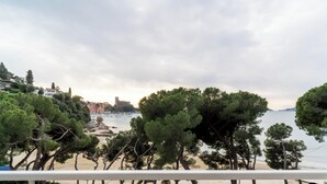 Un balcón con vistas a una playa, árboles y un paisaje urbano distante.