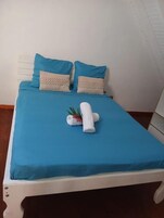 A bed with a blue bedspread, two pillows, and a rolled towel with a plant.