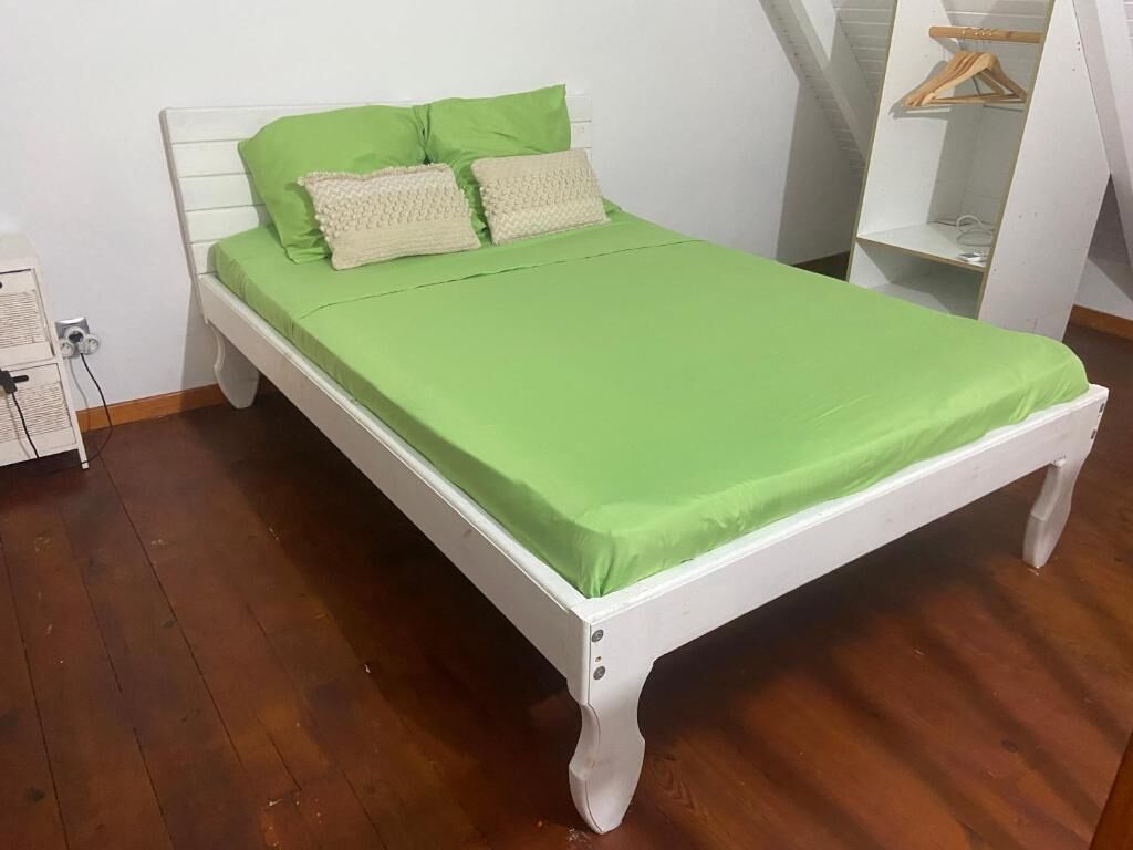 A bed with a green bedspread and two pillows, a white headboard, and a wooden floor.