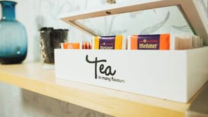Een witte doos met de tekst 'Thee in vele smaken' met theezakjes op een plank.