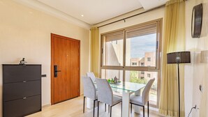 A modern dining area with a glass table, four chairs, a wooden door, and a large window with curtains. - Cozy apartment with pool in Argan, 3 bedrooms (Marrakesh)