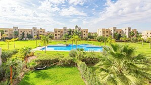 A hotel with a swimming pool surrounded by lush greenery and palm trees. - Cozy apartment with pool in Argan, 3 bedrooms (Marrakesh)