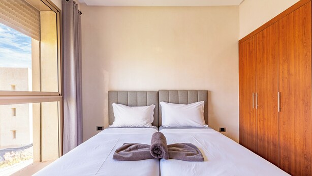 A hotel room with two beds, a wooden wardrobe, and a large window with curtains. - Cozy apartment with pool in Argan, 3 bedrooms (Marrakesh)
