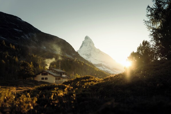 A mountain landscape with a house and a prominent peak in the background.