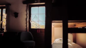 A dimly lit room with a bunk bed, a chair, and a window with a mountain view. - Grünsee Mountain Lodge (Zermatt)