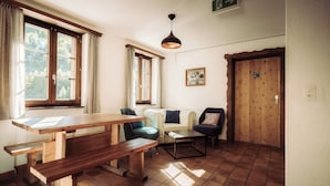 A cozy room with a wooden table, benches, a sofa, and a chair. There is a door with a sign, a framed picture on the wall, and a hanging light fixture. - Grünsee Mountain Lodge (Zermatt)