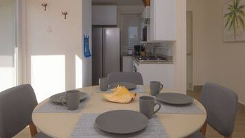 A dining area with a round table, six chairs, and a kitchen in the background.