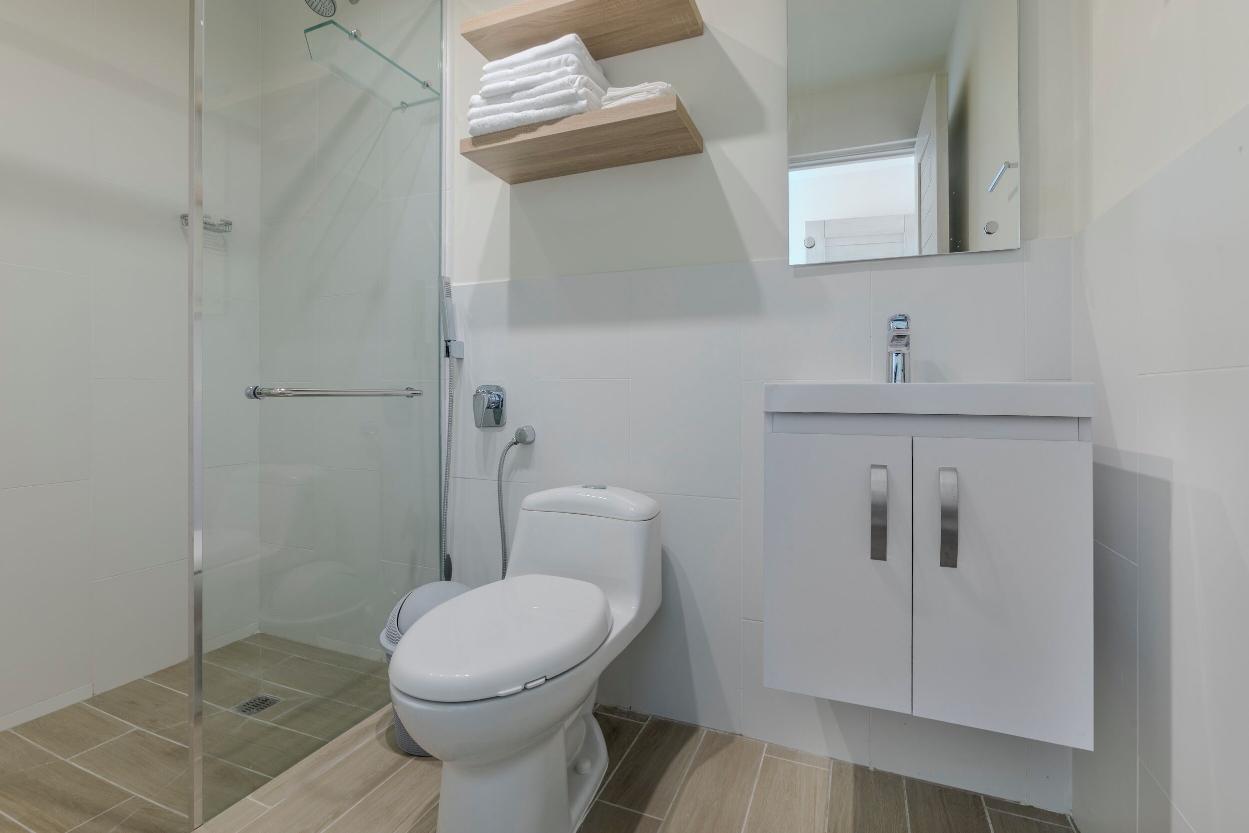 A modern bathroom with a glass shower enclosure, a white toilet, and a white vanity with a mirror.
