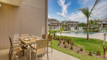 Un patio con una mesa y sillas de madera, una piscina y vistas a edificios residenciales.