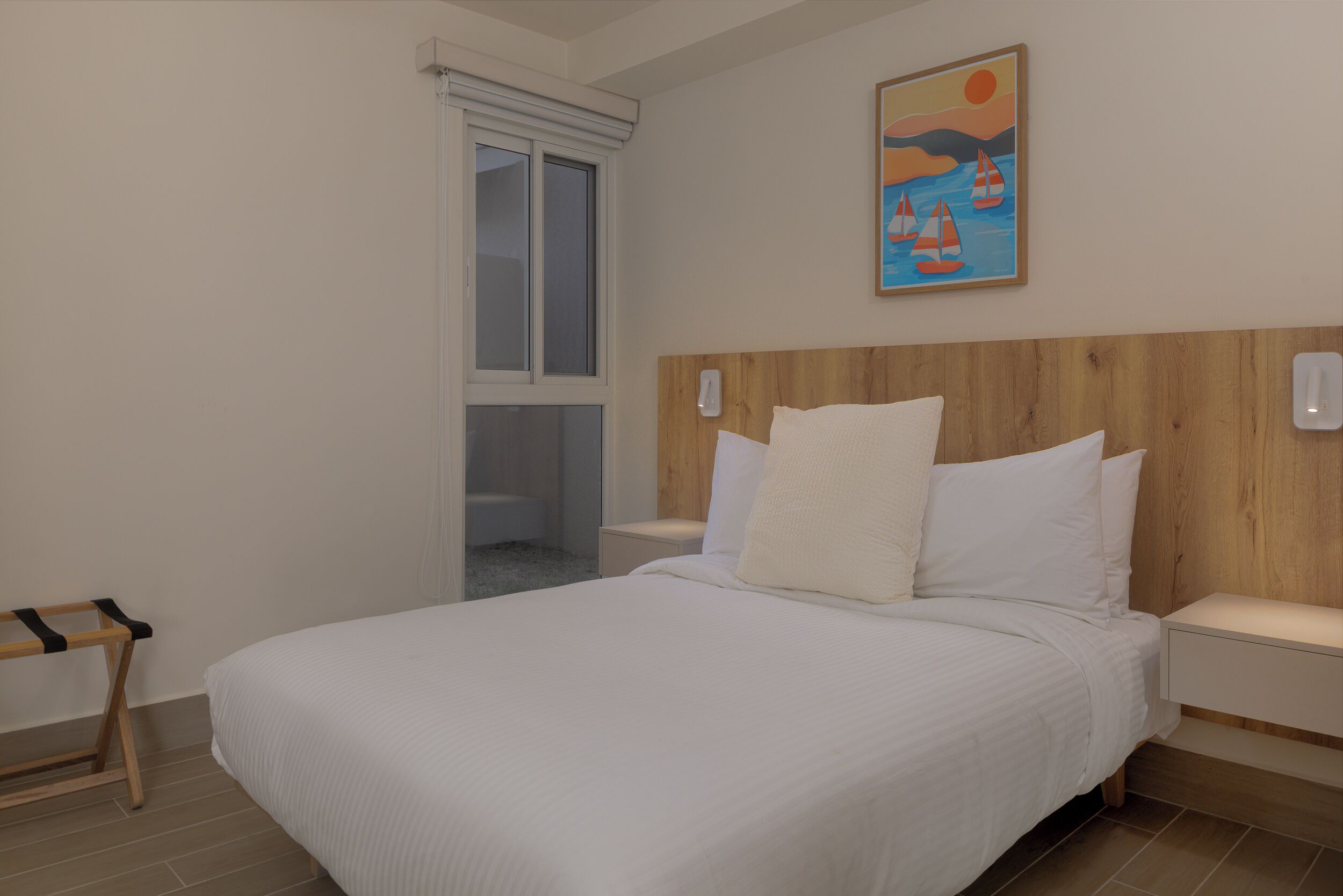 A bedroom with a large bed, a wooden headboard, a nightstand, a window with a view, and a painting on the wall.
