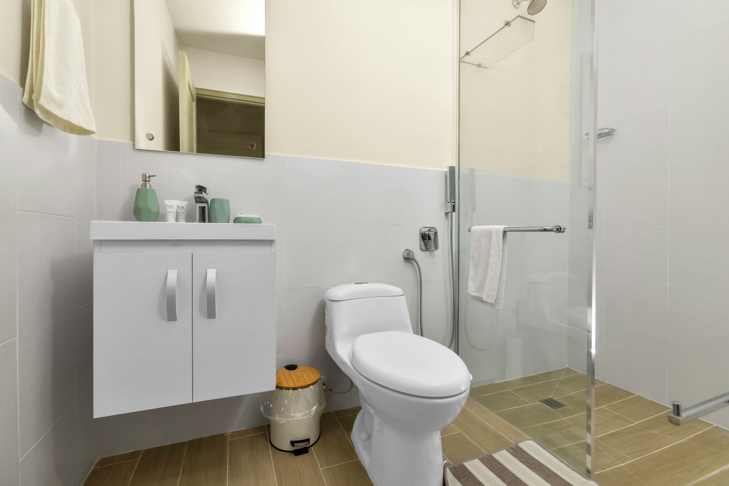 A modern bathroom with a toilet, a sink with a cabinet, a shower area, and a mirror.