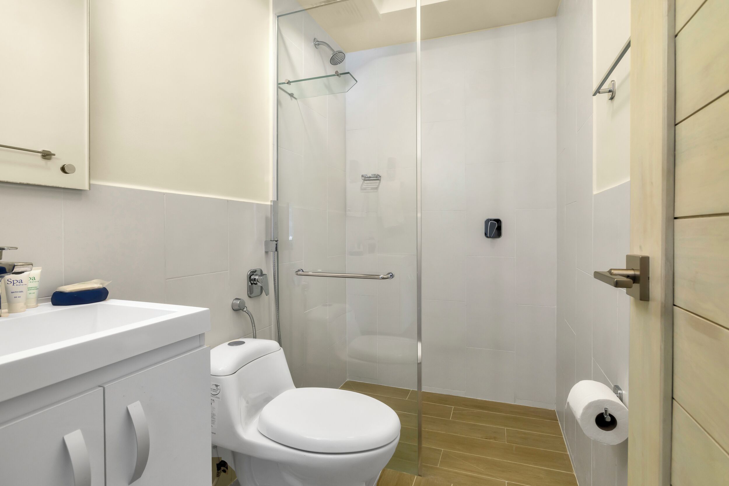 Un baño moderno con ducha acristalada, inodoro blanco y lavamanos con artículos de aseo.