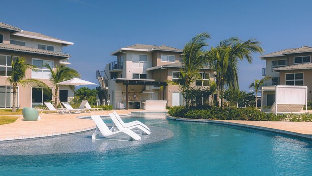 Piscina con sillas de descanso y palmeras, rodeada de edificios de varios pisos.