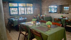 Un restaurante con paredes de ladrillo, varias mesas con manteles verdes y plantas en macetas.