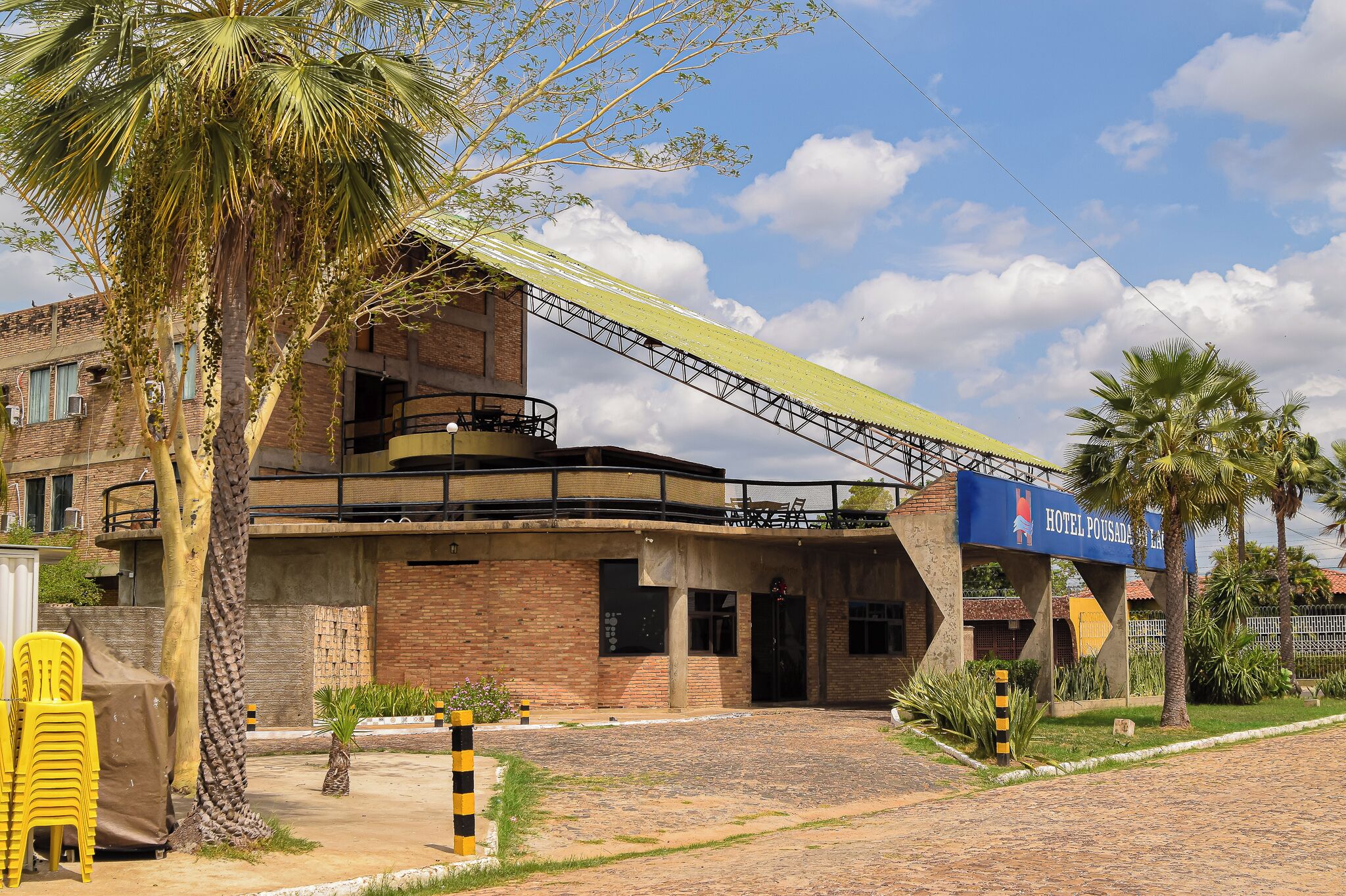 Un hotel con un paseo techado, palmeras y fachada de ladrillo.
