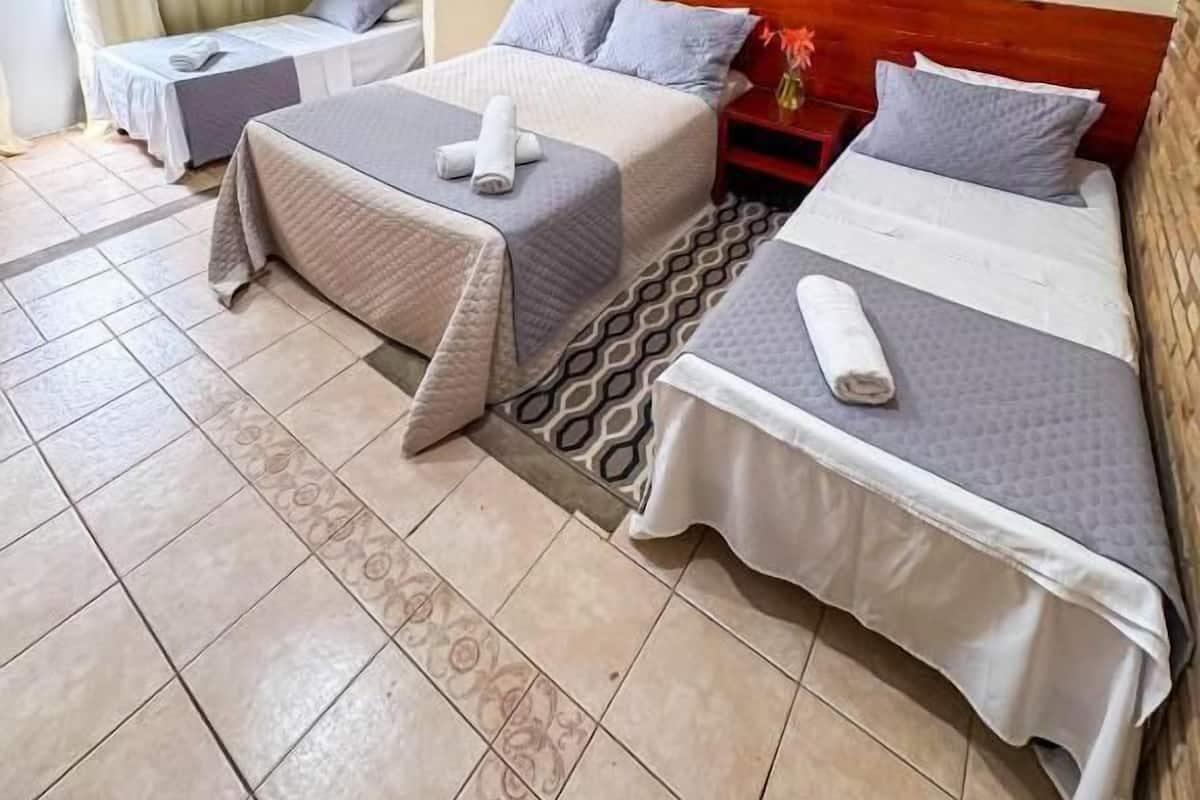 A hotel room with two beds, a small table, a chair, and an air conditioning unit.