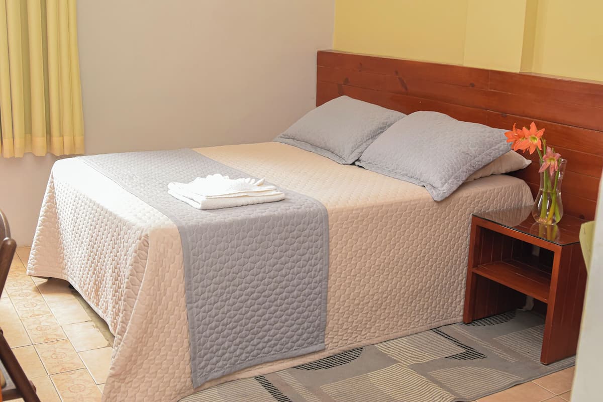A neatly made bed with a quilted bedspread, pillows, and a folded towel.