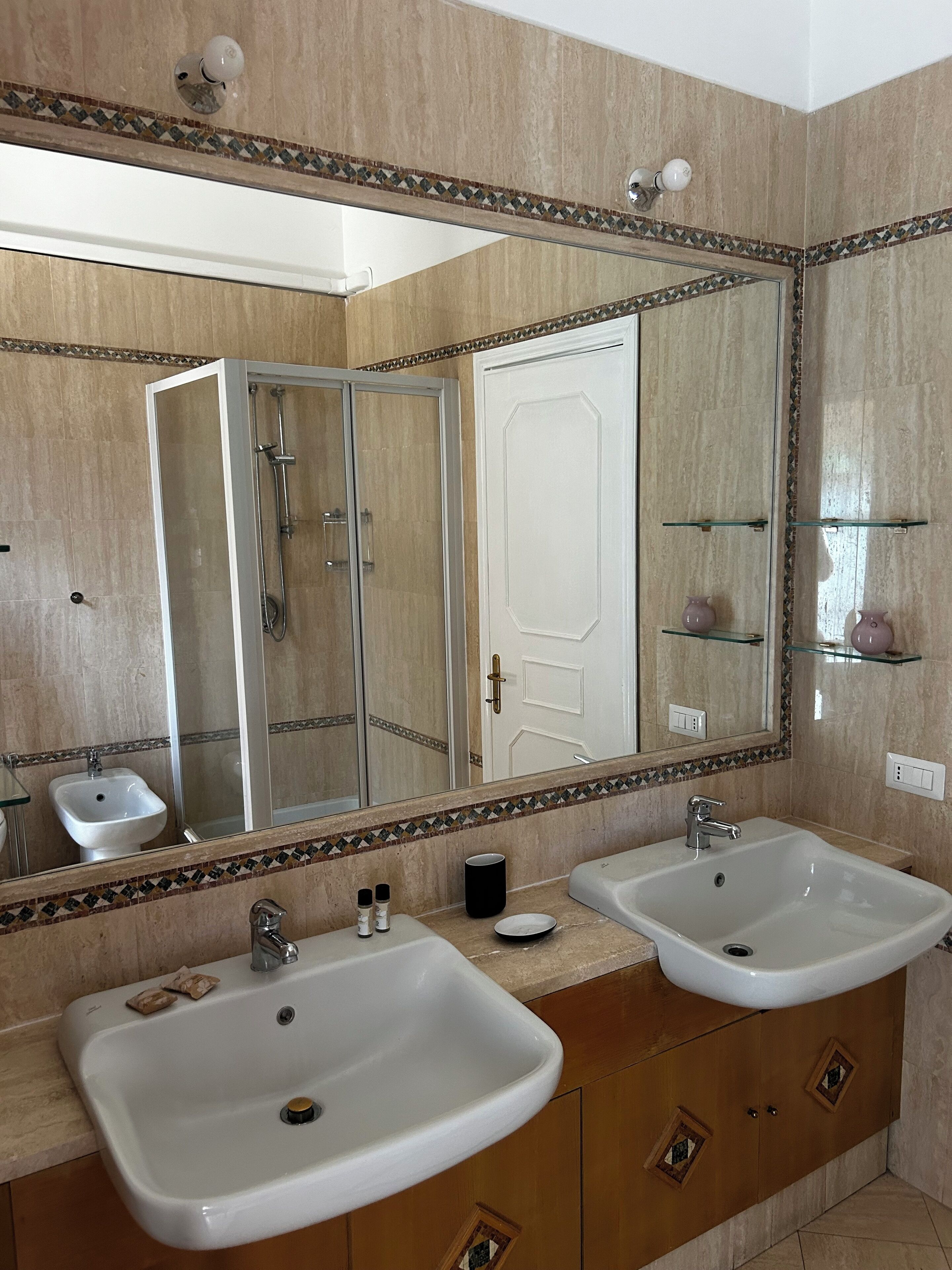 Een badkamer met twee wastafels, een douche en een grote spiegel.