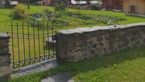 Un borgo rurale con case tradizionali, un muro in pietra e montagne sullo sfondo.