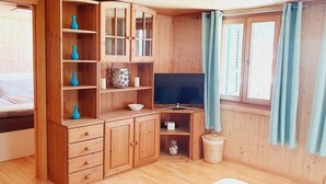 Una stanza in legno con un letto, una televisione, scaffali con oggetti decorativi e una finestra con tende.