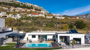 A modern house with a swimming pool, outdoor seating, and a view of a hillside village. - NEW! Villa Bella Ciao: A Stylish 3-Bedroom Retreat with Spectacular Split and Sea Views (Klis)
