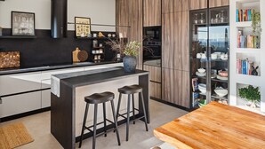 A modern kitchen with a central island, bar stools, a built-in oven, and a bookshelf with decorative items. - NEW! Villa Bella Ciao: A Stylish 3-Bedroom Retreat with Spectacular Split and Sea Views (Klis)