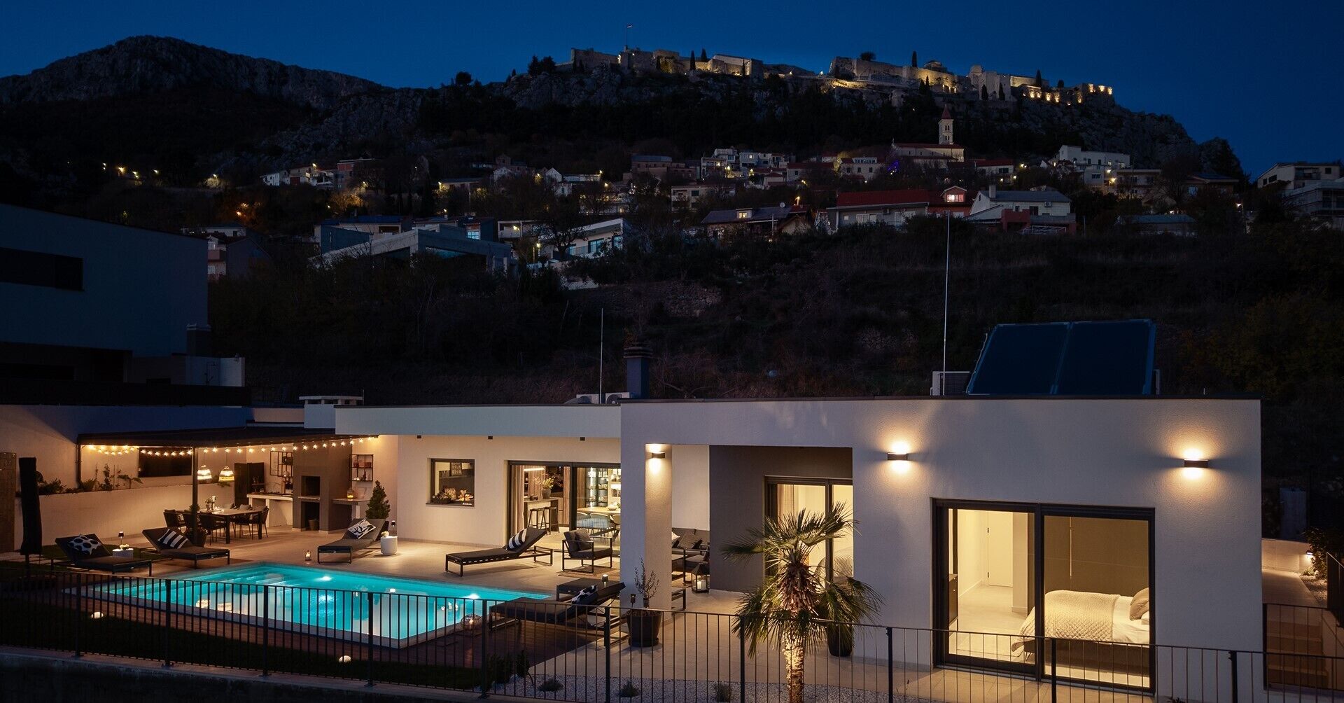 A modern villa with a swimming pool, outdoor seating, and a view of a historic hilltop town.