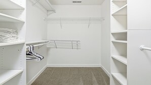 A walk-in closet with white shelves, a metal drying rack, and a carpeted floor.