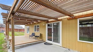 A covered patio with a wooden deck, outdoor seating, and a sliding glass door leading to a backyard.