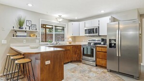 A modern kitchen with a central island, wooden cabinets, stainless steel appliances, and a large refrigerator.