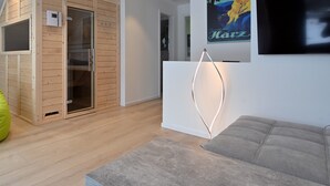Ein modernes Wohnzimmer mit grauem Sofa, Holzboden, integriertem Kleiderschrank und einem Wand-Fernseher.