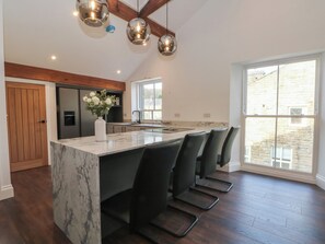 A modern kitchen with a marble island, black bar stools, and pendant lighting. - The Penthouse at 86 (Rossendale)