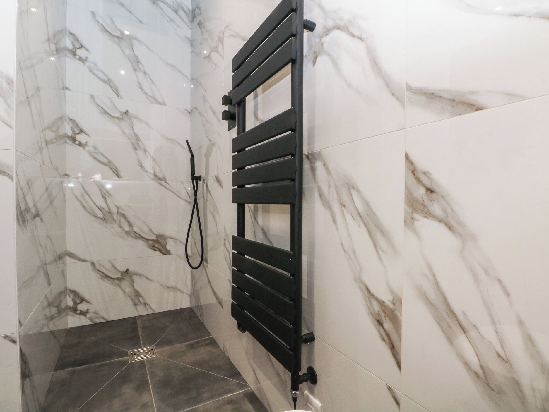 A bathroom with white marble walls and a black towel rack.
