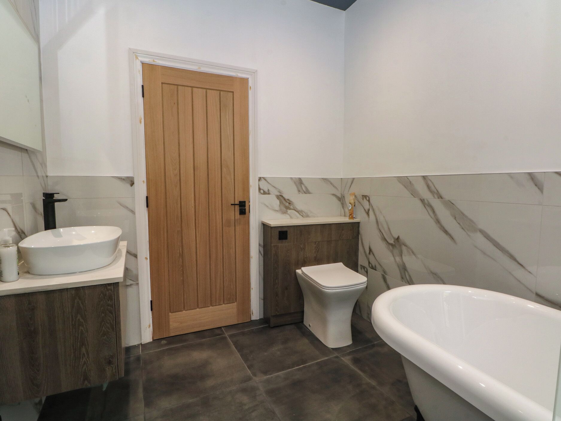 Un baño con puerta de madera, un lavamanos blanco, un inodoro y una bañera.